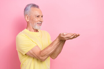 Wall Mural - Photo of candid sincere man with beard dressed yellow t-shirt plams presenting offer look empty space isolated on pink color background