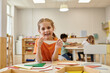 © LIGHTFIELD STUDIOS - positive child holding wooden triangle and looking at camera in montessori school