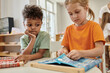 © LIGHTFIELD STUDIOS - african american boy looking at friend playing with cloth and buttons in montessori school