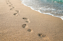 Footprints Of Human Feet On The Sand Near The Water On The Beach