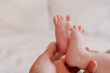 Close Up Of Loving Father Hand Holding Feet, Tiny Toes Of New Born Baby. Unrecognizable Father Touches Barefoot Legs Of 0-6 Child, Enjoy Bonding. Moments With Infant Feeling Unconditional Love Concept