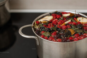 A full pot of hot homemade stewed fruit from various seasonal berries, raspberries, blackberries, apples, pears, basil. Close-up. The pot is on the stove.