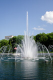 Fototapeta Tęcza - A pond with working fountains, surrounded by a monument of trees and lawn