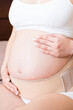 © sosiukin - closeup pregnant woman dresses bandage on belly at home on bed. Orthopedic abdominal support belt