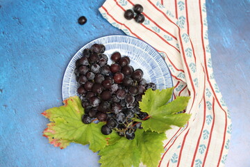 Sticker - Bunch of black grapes on a napkin on a blue background