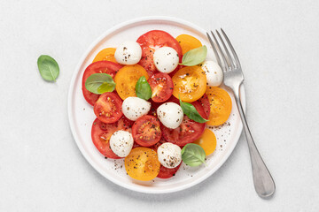 Wall Mural - Appetizing Italian caprese salad. Tomatoes mozzarella basil salad close-up view on white background