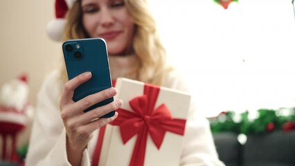 Sticker - Young blonde woman using smartphone holding christmas gift at home