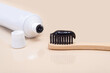 White tube with black toothpaste and a bamboo brush with black bristles on a beige background.