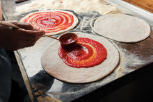 A Man Spreads Italian Tomato Paste Over The Dough, Part Of The Pizza Preparation Process At The Family Café