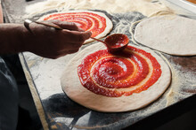A Man Spreads Italian Tomato Paste Over The Dough, Part Of The Pizza Preparation Process At The Family Café