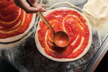 Wall Mural - A woman adds tomato paste to the dough, preparing pizza for baking in a restaurant