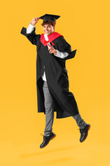 Canvas Print - Male graduate student with diploma jumping on yellow background