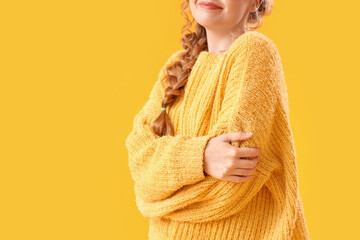 Wall Mural - Young woman in warm sweater and eyeglasses hugging herself on yellow background