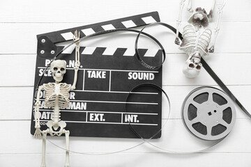 Clapperboard with film reel and skeletons on white wooden background. Halloween celebration