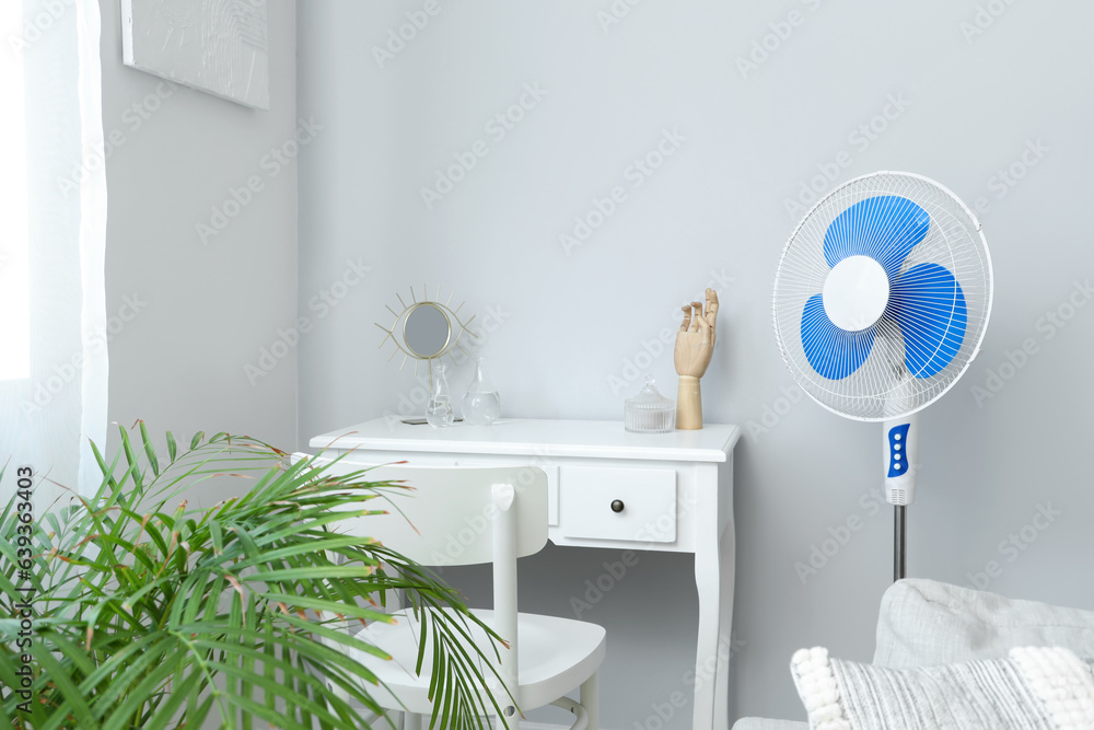 Interior of light room with floor fan near white dressing table