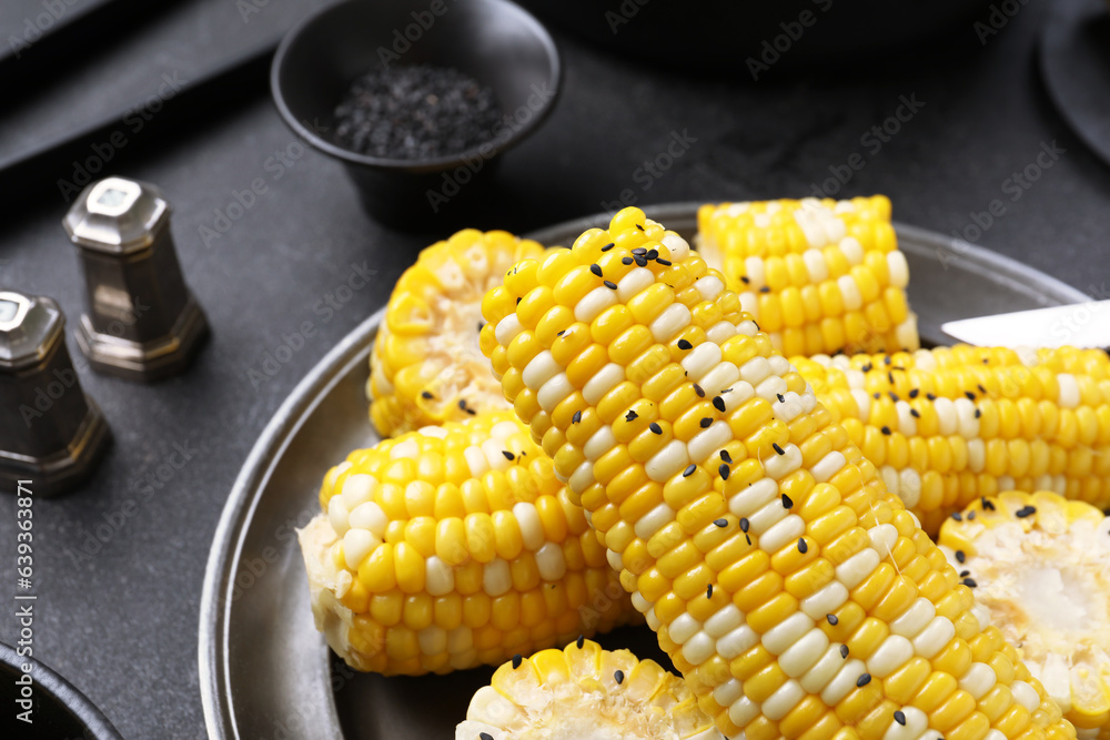 Plate with boiled corn cobs on black background