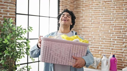 Sticker - Young latin man holding basket smelling clean clothes at laundry room