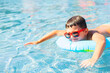 Cute baby boy in red sunglasses swims with a rainbow inflatable ring in a clean pool