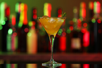 Martini glass with cocktail, ice cubes and rosemary on counter in bar