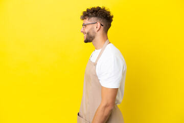 Wall Mural - Restaurant waiter blonde man isolated on yellow background laughing in lateral position