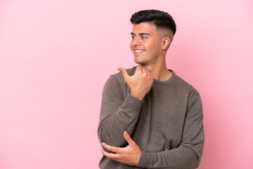 Wall Mural - Young caucasian handsome man isolated on pink background pointing to the side to present a product