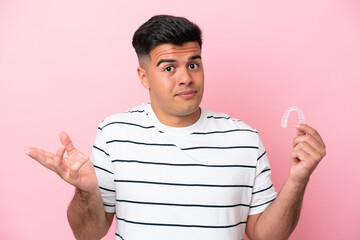 Wall Mural - Young caucasian man holding invisaling isolated on pink background making doubts gesture while lifting the shoulders