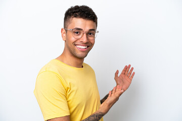 Wall Mural - Young Brazilian man isolated on white background With glasses and presenting something