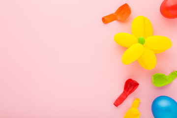 Wall Mural - Beautiful flower head created from yellow balloon. Colorful deflated balloons on light pink table background. Pastel color. Closeup. Making different shapes. Empty place for text. Top down view.