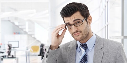 Canvas Print - Confident businessman smiling in modern business office. Portrait of young adult man in 30s, happy confident smile. Copy space.