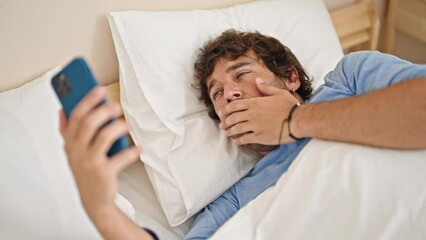 Wall Mural - Young hispanic man using smartphone lying on bed tired at bedroom