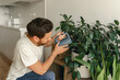 © Daria - Smiling mature man in casual clothes watering plants at home. Housework and household concept