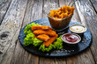Fried fish sticks with French fries and fresh vegetables on wooden table
