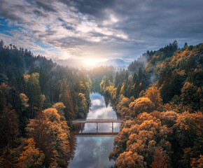 Wall Mural - aerial view of wooden bridge over the river in mountains at foggy autumn morning in slovenia. top dr