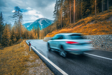 Wall Mural - blurred car in motion on the road in orange forest in rain in autumn. dolomites, italy. perfect moun