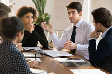 Poster - Multiracial businesspeople sit at desk in office talk brainstorm discuss business project at meeting together, focused diverse colleagues engaged in team discussion at briefing, collaboration concept