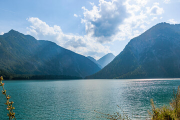 Evening sun rays through clouds on blue sky over Plansee lake in Austria