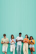 © Jose Calsina - Vertical. Group of multiethnic teenagers addicted to use smartphone on blue background. multiracial young people or students, watching their cell phone and sharing media on a teal wall. Copy Space