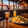 Plato con patatas fritas y varios refrescos de naranja y cola sobre una mesa en un bar con terraza
