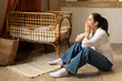 © Home-stock - Young caucasian tired woman sitting on the floor near children's cot, baby sleeping in her cradle. Postnatal depression and stressful motherhood concept