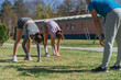 © qunica.com - Low angle view shot of two elastic girls doing fold pose. Their male fitness instructor is watching them. Workout in the park