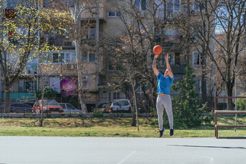 Wall Mural - Young male basketball player shooting for 3 points. He is training at the basketball court in the city