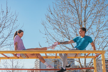 Wall Mural - Sports girl showing her new sneakers to her boyfriend and smiling. They are sitting on horizontal metal bars in the city