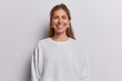 Portrait of cheerful long haired woman smiles toothily being in good mood dressed in casual sweatshirt has piercing in nose isolated over white background. People postive emotions and feelings concept