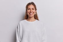 Portrait Of Cheerful Long Haired Woman Smiles Toothily Being In Good Mood Dressed In Casual Sweatshirt Has Piercing In Nose Isolated Over White Background. People Postive Emotions And Feelings Concept