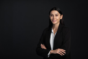 Close-up of an attractive business woman with toothy smile staning at isolated dark background, copy space.