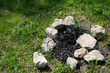 fire pit with river stones and brunt out charcoal on the grass in summer  