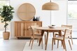 Natural wood round dining table and chairs on wicker rug. Wooden cabinet in dining room. Scandinavian style home interior design