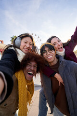 Vertical selfie cheerful two couple walking outdoor amusement park and having fun celebrating excited vacations. Young happy people piggybacking their friends in sunny. Leisure and freedom in winter.