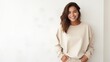 © Fred - beautiful woman wearing a plain tan sweatshirt standing in front  white wall with modern decor in the background in a happy mood