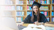 © EduLife Photos - An asian girl student in university graduate gown with books, laptop studies happily in library.